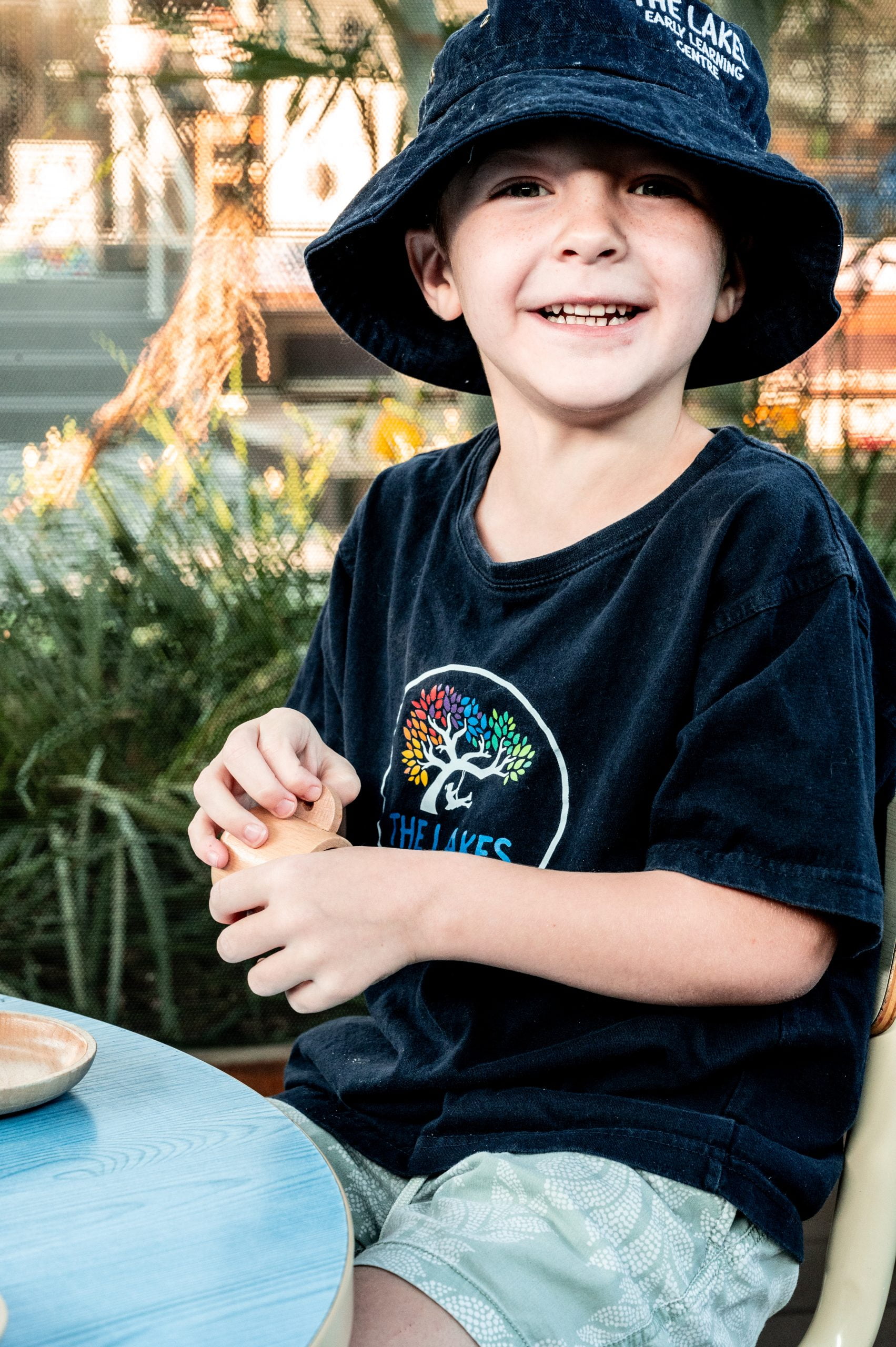 A young boy, enrolled at The Lakes Early Learning Centre, is sitting at a table with a hat on.